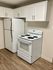 Modern kitchen with white cabinetry, electric stove, and refrigerator, featuring elegant wood flooring.
