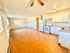 Bright open kitchen with white cabinetry, appliances, and wooden flooring extending into a spacious living area.