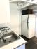 Efficient kitchen space with a stainless steel sink, gas stove, white fridge, and compact microwave.