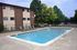 Inviting outdoor swimming pool with lounge chairs beside a brick apartment building, surrounded by lush trees.