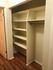 Well-organized open closet with multiple shelves and a hanging rod, accentuated by warm wooden floors.