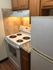 Compact kitchen with electric stove, granite countertop, wooden cabinets, and tiled backsplash.