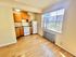 Bright kitchen with wooden cabinets, a stove, a refrigerator, and a large window offering city views.