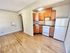 Bright kitchen area with wooden cabinets, a white stove, and refrigerator next to an open space with hardwood floors.