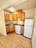 Compact kitchen with wooden cabinets, a stove, refrigerator, and tiled backsplash.