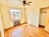Empty bedroom with sunlit wooden flooring, a ceiling fan, and a large window overlooking the city.