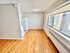 Sunlit small kitchen area with sleek hardwood flooring and a large window overlooking a brick building.