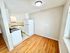 Bright kitchen area with white cabinets, stove, and refrigerator, adjacent to an open space with hardwood floors.