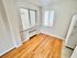 Bright room with wooden floors and large windows, featuring a classic white refrigerator.
