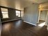Room with dark wooden flooring, large windows bringing in natural light, and a doorway leading to another area.