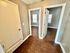 Bright hallway with wooden flooring leading to two open rooms with natural light.