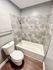 Sleek bathroom with modern tiles, a white bathtub, and toilet on wooden flooring.