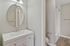Elegant bathroom featuring modern vanity with a round mirror, seamless shower space, and warm wood flooring.