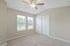 Bright and spacious bedroom with soft carpet, large windows, and ceiling fan, offering a serene and inviting atmosphere.