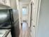 Bright and narrow kitchen hallway featuring sleek black appliances and modern cabinetry, leading to a well-lit bathroom.