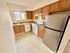 Bright, modern kitchen with stainless steel fridge, ample wooden cabinets, and natural light from a large window.