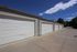 Row of modern garages with pristine white doors under a clear blue sky, offering secure and spacious parking.