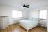 Bright and inviting bedroom with wooden floors, a cozy bed, modern ceiling fan, and ample natural light from large windows.
