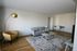 Bright and spacious living room with modern furnishings, featuring a gray sofa, stylish armchair, and sleek coffee table on a textured rug.
