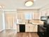 Bright modern kitchen with sleek white cabinets, black appliances, and wood flooring, featuring double sinks and ample counter space.