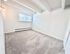 Bright and airy bedroom with soft carpet flooring, large window for natural light, and contemporary light fixture.