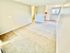 Bright and inviting open-concept living area with plush carpeting, leading to a cozy kitchen with white cabinetry and large window.