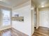 Bright, airy apartment entryway with sleek wood flooring and modern kitchen design, showcasing natural light from large windows.