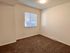 Bright and inviting empty room with plush carpeting, large window, and soft lighting.