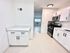 Bright and modern kitchen with sleek white cabinets, stainless steel appliances, and elegant countertops, leading into a sunlit living space.