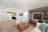 Inviting open-concept living room with contemporary furniture and a cozy rug, adjacent to a well-equipped kitchen with wooden cabinets and modern appliances.