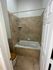 Modern bathroom featuring elegant beige tile, a relaxing bathtub, and a stylish wooden toilet seat.