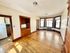 Warm, sunlit living room featuring classic hardwood floors, elegant built-in shelving, and large bay windows. Adjacent kitchen offers modern convenience with a stylish finish.