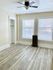 Bright and airy room with elegant gray wood flooring, large windows with blinds, and modern ceiling fan.