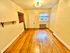Bright empty room with polished hardwood floors, a single window, and a minimalist light fixture, offering a cozy and inviting atmosphere.