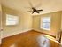 Bright and inviting empty room with polished hardwood floors, two sunlit windows, and a classic ceiling fan.