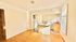 Bright empty apartment dining area with wood flooring, adjacent compact kitchen featuring a fridge and natural light flowing in through large windows.