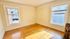 Bright, sunlit room with hardwood floors and two large windows, offering a cozy and inviting atmosphere.