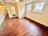Bright room with polished wooden flooring, large windows for natural light, and direct access to a hallway and bathroom.