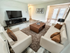 Modern living room with sleek white sofas, a large flat-screen TV, and elegant decor, showcasing a bright and inviting space with natural light.
