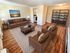 Inviting living room with cozy leather seating, open bookshelf, and warm wood flooring, exuding comfort and style.