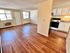 Bright and inviting open-plan living area with wood flooring, adjacent to a modern kitchen with sleek appliances.