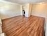 Spacious living area with elegant wood flooring and neutral walls, leading to a cozy kitchen.