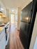 Charming narrow kitchen with modern appliances, sleek black refrigerator, and inviting wood flooring leading to a sunlit hallway.
