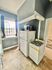 Cozy kitchen with natural light, featuring a compact layout with a white refrigerator, small gas stove, and bright window with curtains.