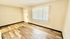 Bright, inviting empty room with elegant wood flooring, large window allowing natural light, and neutral-toned walls.