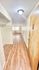 Welcoming apartment entryway with stylish wood flooring and bright overhead lighting leading to a cozy living area with large window.