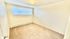 Bright and cozy empty room with plush carpeting, large window, and ceiling light fixture, ready for personalization.