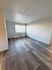 Bright, spacious room with modern wood flooring and large window for natural light.