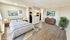 Bright and airy bedroom with modern decor, large windows, and an open layout leading to a cozy kitchen and living space.