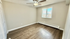 Bright and spacious bedroom with modern wood flooring, neutral walls, and large window with vertical blinds.